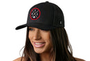 A smiling woman with long brown hair wears the Haka Hat Atlanta Trucker Hat, a black mesh ATL X Football Snapback by Haka Hat with a red and white circular ATL X patch logo, against a white background.