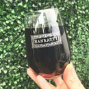 A hand holds a Swanky Badger Stemless Wine Glasses - Set of 4: The Modern, personalized with the name HANRATTY inside an ornate rectangular frame and filled with red wine.