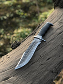 The Texan Knives Best Bowie Knife, featuring a 13" handmade Damascus steel blade and resin horn handle, rests on a weathered tree trunk outdoors with a blurred natural background.