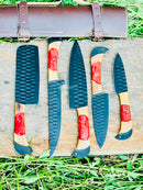 The Texan Knives Best Japanese Kitchen Knife Set includes a 13" forged stainless steel chef knife with an olivewood and resin handle, plus a leather sheath, beautifully displayed on a wooden board outdoors amidst green grass.