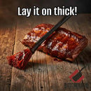 A rack of ribs on wood is glazed with sauce using the Butcher BBQ Mop Brush. Text: Lay it on thick! The Butcher BBQ logo appears in the bottom right corner.