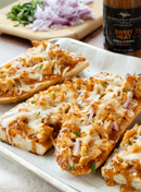 Toasted bread halves with shredded chicken, melted cheese, red onion, and herbs on a tray. In the background: chopped onions, greens, and a Terrapin Ridge Farms Sweet Heat Grill & Wing Squeeze bottle.