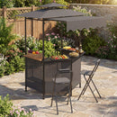 Outdoor patio featuring the DirectDeals Grill Gazebo with Shelves, Hooks & Double Roof Canopy, two stools, and a counter with fruit, snacks, and drinks on a stone-paved area surrounded by lush greenery and flowers.