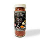 A clear plastic jar with a white lid, labeled SALTOPIA Infused Sea Salts BBQ Salt: MEAT HEAD, contains reddish-brown Texas BBQ seasoning—ideal for authentic barbecue rubs. The label displays small bowls of sauces and spices.