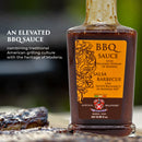 A bottle of Taycte Aged Balsamic Steak Sauce — made with 25-30 Year Balsamic Vinegar of Modena — sits on a table beside grilled meat. The label displays ornate designs with text that emphasizes its Italian roots and American grilling inspiration.