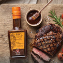 Taycte Aged Balsamic Steak Sauce — with 25-30 Year Balsamic Vinegar of Modena in a bottle, slices of grilled steak, a bowl of Taycte Aged Balsamic Steak Sauce with a brush, and rosemary garnish arranged on a wooden board.