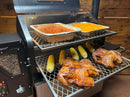 A Pimp My Grill® Gen2 Slide-Out Rack System - 2 Racks for Green Mountain Grills Ledge / Daniel Boone holding two roasted chickens, four ears of corn, and two foil pans of baked beans on its dual-level metal racks.