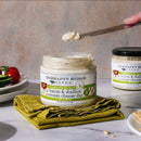 An open jar of Terrapin Ridge Farms Bacon & Scallion Cream Cheese Dip sits on a green napkin, with a knife and snacks nearby—making it an ideal appetizer for parties. Another closed jar is visible in the background.