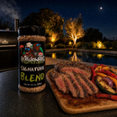 A bottle of BuffalowBBQ Signature Blend BBQ Rub next to a wooden cutting board with sliced steak and grilled vegetables.