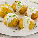Five baked potatoes with creamy white sauce, chopped cucumber, and fresh herbs, sprinkled with SALTOPIA Infused Sea Salts’ Bacon & Ranch Seasoning: HOWDY DO, served on a white plate.