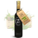 A dark bottle of Georgetown Olive Oil Co. GREEN CHILI | High Polyphenols Extra Virgin Olive Oil, labeled with a kraft tag, is displayed in front of a wooden crate filled with fresh green chili peppers.