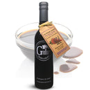A bottle of Georgetown Olive Oil Co. 18 YEAR AGED Balsamic Vinegar Reduction, featuring a tan label, stands in front of a glass bowl filled with the rich, dark vinegar; some of the aged balsamic reduction is artfully spilled beside the bottle.