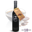 A dark bottle of Georgetown Olive Oil Co 18 YEAR AGED Balsamic Vinegar Reduction with a tan tag stands in front of a bowl of vinegar and a few drops. Text reads "AGED 18 YEARS." The label features the Georgetown Olive Oil Co. brand, Washington, DC.