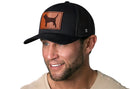 A smiling man wears the Haka Hat Beagle Trucker Hat Leather, a black dog snapback by Haka Hat, paired with a beige t-shirt and shown against a white background.