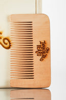 A Wooden Beard Comb from The Immaculate Beard, engraved with the brand’s name, rests against a light-colored wooden surface—making it the perfect accessory for any beard grooming routine.
