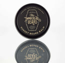 A round tin labeled The Immaculate Beard Sunset Beard Balm, included in the Immaculate Premium Beard Grooming Gift Set For Men Complete Care Kit by The Immaculate Beard, stands on a reflective surface and features scents of citrus peel, vanilla musk, and tonka bean.