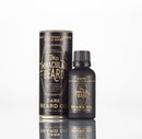 A sleek black bottle labeled “The Immaculate Beard Conditioning Natural Beard Oil” stands beside its coordinating cylindrical case. Both feature gold and white lettering, showcasing notes of tobacco blossom, caramel, rose, and honey. Ideal for nourishing your beard on its own or pairing with your favorite beard conditioner or natural beard balm for a complete grooming regimen.