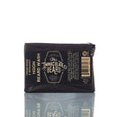 A black-wrapped bar of The Immaculate Beard Natural Beard Wash Bar | Beard Shampoo with a cedar wood and bourbon scent, featuring gold and white text on the label, is displayed against a white background with a reflection below—an elevated natural beard care choice from The Immaculate Beard.