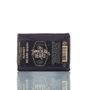 A rectangular bar of Immaculate Beard Natural Wash Bar For Men Deep Clean is wrapped in black paper with a label displaying The Immaculate Beard brand name along with product and ingredient details. This natural beard wash contains activated charcoal for a deep clean, and its vintage-style packaging lends it a timeless appeal.