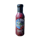 A bottle of Big Wick's Blueberry Jalapeno Glaze by Big Wick's rests on a wooden surface outdoors, with a blurred, vibrant sunset and green scenery in the background, capturing authentic Southern BBQ flavor.