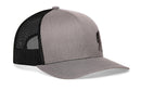 The Haka Hat Bigfoot Trucker Hat in gray-black features a curved brim, black mesh back panels, and a subtle Sasquatch logo on the front left panel, shown from a front-side angle.