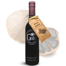 A bottle of Georgetown Olive Oil Co. BLACK GARLIC Balsamic Vinegar | Barrel Aged, Modena Italy is positioned in front of a whole black garlic bulb and a cross-section of garlic, with a gold tag tied around its neck. Produced by Georgetown Olive Oil Co., this exceptional balsamic vinegar is made with barrel aged balsamic from Modena, Italy, offering rich and complex flavors in every drop.