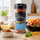 A jar of Texan Heartland Blackened Seafood Seasoning by Texan Heartland rests on the kitchen counter beside a bowl filled with shrimp, fresh lemon wedges, garlic, and vibrant herbs. Sunlight pours through the window behind, creating an inviting atmosphere for preparing high-heat seafood dishes packed with bold Gulf Coast flavor.