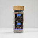 A Spice Wheel Blueberry Sugar jar from the Spice Wheel brand, featuring a wooden lid and label, holds 100g of a blend of granulated sugar and blueberry powder. The glass container is displayed on a white surface against a simple background.