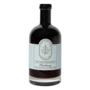 A glass bottle of Under The Bark Syrup Co Blueberry Maple Syrup with a black cap and a white label featuring a maple leaf illustration.