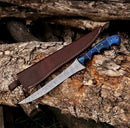 The Texan Knives 8" Handmade Rasp Steel Sheep Horn Hunting Knife, featuring a blue handle and patterned blade, rests on tree bark beside its sturdy leather belt sheath.