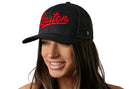 A woman with long brown hair smiles while wearing the Haka Hat Boston Red Script Trucker Hat, a black Massachusetts snapback by Haka Hat. "Boston" is written in red script on the front against a plain white background.