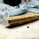 Close-up of the Spaceman Knives Interstellar Bread Knife featuring a wooden handle and AUS-10 steel ends, resting on a light textured surface with soft blue-gray fabric in the background.