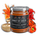 A 9oz jar of Harmacy Hot Sauce Co. Brimstone Inferno Extra Hot Tahini & Roasted Red Pepper Sauce is displayed with roasted red peppers, a red chili, tahini, and orange spice powder on a white background.