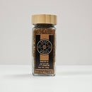 A Spice Wheel glass jar with a wooden lid, labeled "Spice Wheel Brown Za’atar," Net Wt. 64g, contains a rich brown za’atar spice blend made with aromatic thyme.