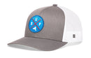 The Haka Hat Buffalo Trucker Hat is a gray and white snapback with a blue circular patch featuring red crossed lines, B-U-F letters, and a buffalo silhouette. The sides and back have breathable white mesh.