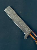 A close-up of the Bull Cutter Knife by Texan Knives, featuring a handmade Damascus steel blade with a wavy pattern and an orange and black Pakkawood handle, set against a dark background.