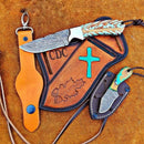 The Texan Knives Bull Sheath Leather Knife features a 4.5" patterned Damascus steel blade and multicolored handle in a decorative sheath with CDC, blue cross, and oak leaf. Includes leather wrist strap and small knife in black sheath.