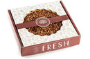 A 9-inch Millican Pecan Southern Bourbon Pecan Pie sits inside a decorative brown and white box with charming pecan illustrations and the word “FRESH” proudly displayed on the front. The clear top lets you admire the golden, bourbon-infused filling and toasted pecans—a true Southern dessert presentation from Millican Pecan.