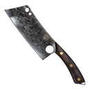 The Spaceman Knives Meteor Series Kitchen Cleaver, featuring a textured stainless steel blade and a wooden handle with brass rivets, rests on a white marble surface beside a folded black cloth.
