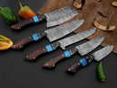The Texan Knives Best Chef Knife Set includes a 13" handmade Damascus steel kitchen knife with a wenge resin handle and leather sheath, displayed on a black surface beside a brown leather roll and vibrant peppers.