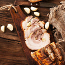 Sliced roasted pork roll with pepper and spices on a wooden board beside garlic cloves—ideal when paired with Saltopia Ultimate Carnivore Salts from SALTOPIA Infused Sea Salts for the ultimate BBQ flavor experience.