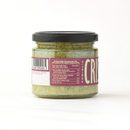 A glass jar with a black lid holds Taycte Famiglia Crispino Artichoke Bruschetta Spread — Marinated Italian Carciofi, a greenish shredded mixture. The label displays nutrition info, barcode, and FAMIGLIA CRIS text.