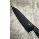 The Spaceman Knives Dark Matter Kiritsuke chef's knife, featuring a textured handle and blade logo, rests on a light gray surface. Crafted from premium 7CR17MOV-X steel for outstanding performance and durability.