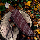The Texan Knives Small Bushcraft Knife features a 9" Damascus steel blade, a rosewood handle, and comes with a leather sheath, shown resting on a tree stump among fallen yellow and orange leaves.