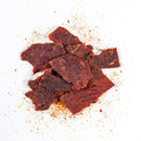 Slices of Chiles & Smoke Sedona Sand Beef Jerky – Southwest Garlic & Chile are arranged in a pile on a white background, with visible seasoning and spice scattered around the pieces, highlighting the signature small-batch Southwest flavor crafted by Chiles and Smoke.