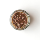 Top view of an open glass jar of Taycte Famiglia Crispino Black Olive Bruschetta Spread — Italian Olive Tapenade by Taycte, filled with a thick, brown, chunky spread perfect for making authentic Italian bruschetta, placed on a white background.