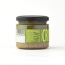 A glass jar with a black lid contains Taycte Famiglia Crispino Green Olive Bruschetta Spread — Tapenade Style Italian, its greenish contents hinting at Mediterranean olive tapenade flavors. The label bears the Taycte brand name, along with a barcode, ingredients list, and nutrition facts. Most of the product name is not visible in the photo. The jar is displayed on a plain white background.