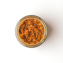 Top view of a glass jar filled with Taycte Crispino Bruschetta Pomodori Secchi — Calabrian Sun-Dried Tomato Spread, a chunky, reddish-brown condiment from Taycte, resting on a white background. This vibrant vegan and gluten-free spread is perfect for those seeking flavorful Calabrian bruschetta toppings.