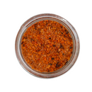 A glass jar of SALTOPIA Infused Sea Salts' Hickory Salt: CABIN FEVER, filled with coarse, orange-brown hickory smoked sea salt, viewed from above on a white background.