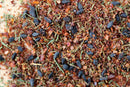 A close-up of World Spice Calico Fish Rub by World Spice, a blend featuring black seeds, dried herbs, reddish-brown flakes, and coarse salt granules mixed together—perfect as a salmon rub.